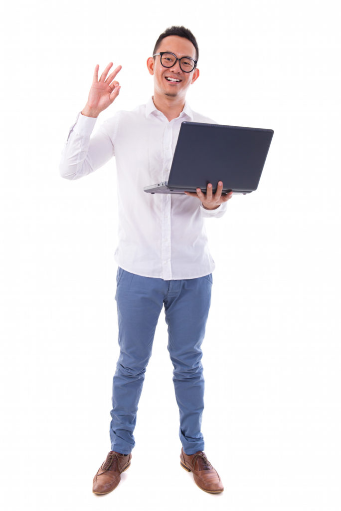 Full length of happy Asian businessman using laptop showing okay hand sign standing isolated over white background